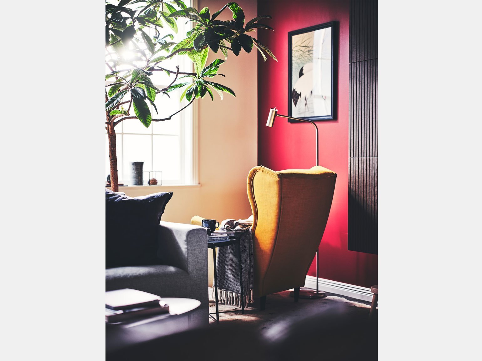 жёлтое кресло с ушами Ikea Strandmon и кофейный столик стоят у окна около ярко-розовой стены